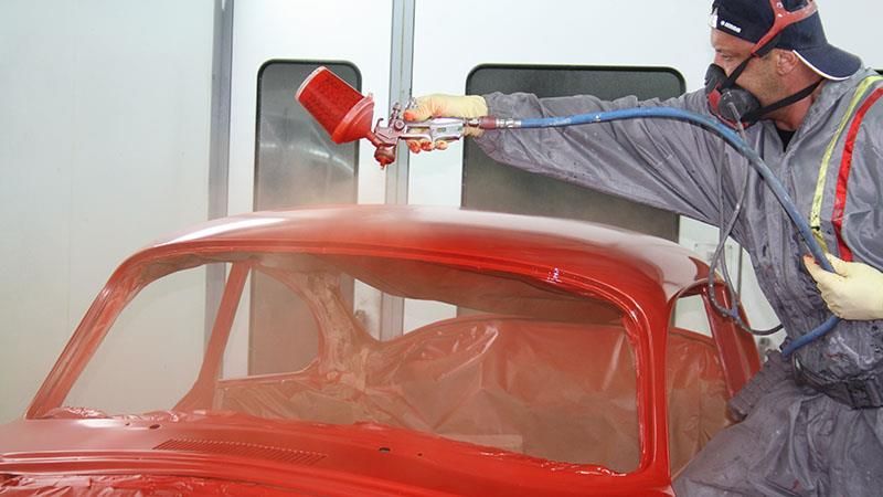 Ein Mann bemalt in einer Garage ein rotes Auto mit Sprühfarbe.