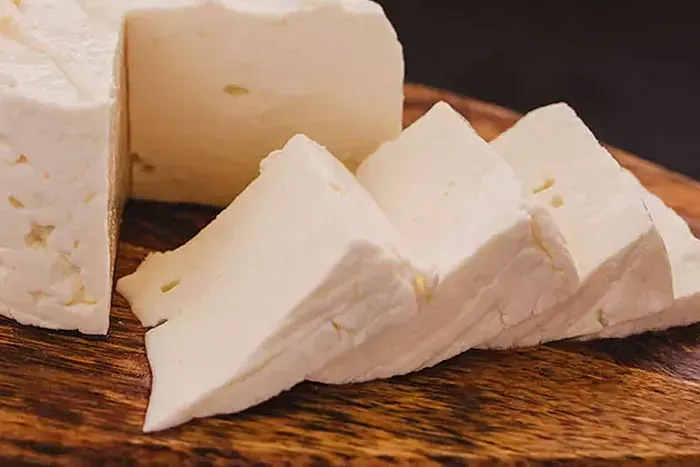 Un trozo de queso blanco reposa sobre una tabla de cortar de madera.