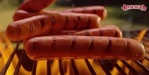 Un montón de perritos calientes se están cocinando en una parrilla.