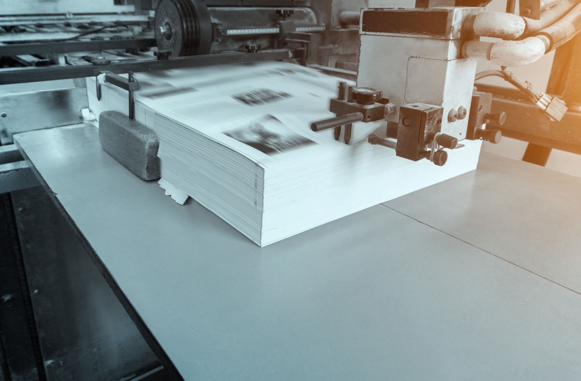 Une machine à imprimer alimente une imprimante avec une pile de papier blanc, sur une surface industrielle grise.