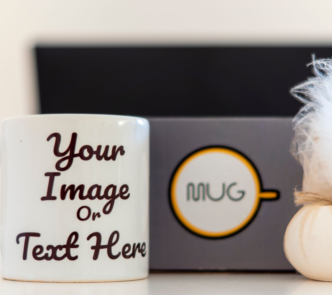 Une tasse blanche sur laquelle est imprimé l'inscription « Votre image ou texte ici » est placée à côté d'une boîte grise ornée d'un logo circulaire portant l'inscription « TASSE ».