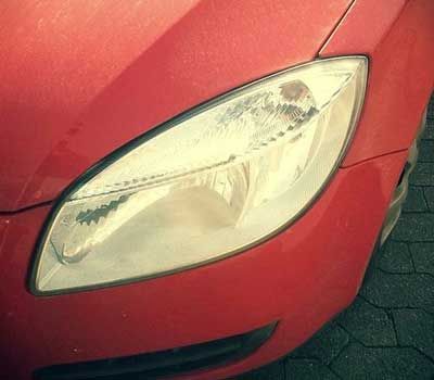 Farol vermelho de carro, em formato de amêndoa, ligeiramente opaco, contrastando com a carroceria vermelha do veículo.