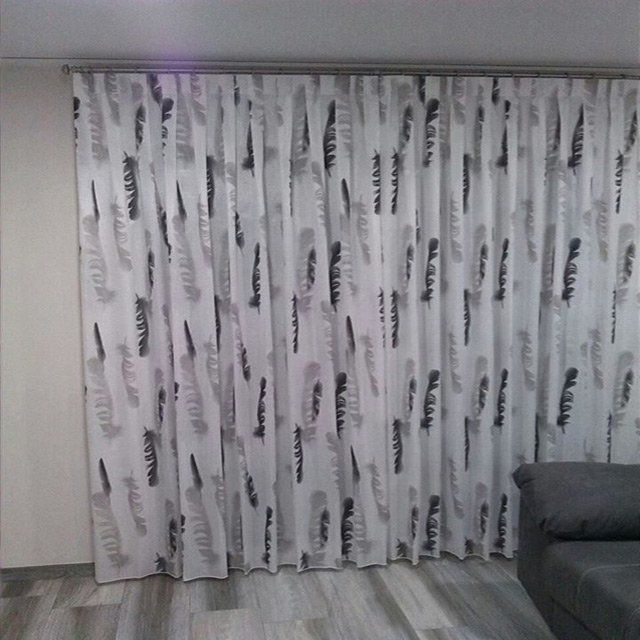 Sala de estar con cortinas blancas estampadas cerradas y un sofá gris a la derecha.