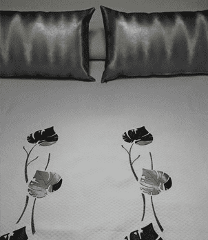 Colcha gris con dos almohadas negras y dos diseños florales en blanco y negro debajo.