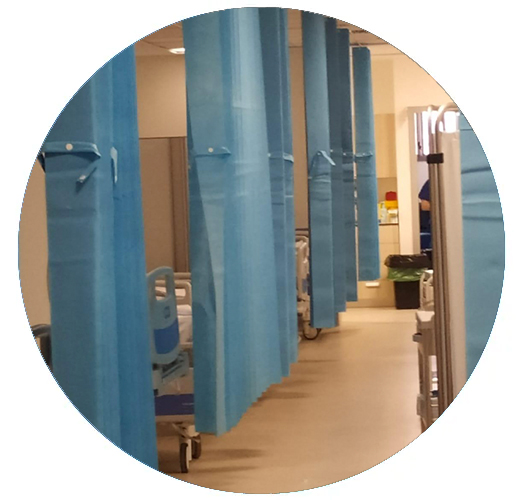 Pasillo de hospital con cortinas azules para mayor privacidad y equipo médico a lo largo de los laterales.
