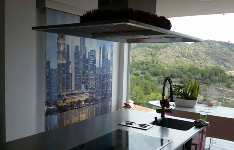 Cocina moderna con encimera negra, ventanal grande, mural con motivos urbanos y vistas a las verdes colinas.