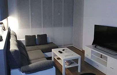 Sala de estar moderna con sofá seccional gris, mesa de centro blanca y televisor sobre un soporte blanco.