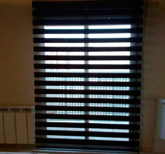 Ventana interior con persianas horizontales oscuras y luz natural brillante que se filtra a través de ella; radiador a la izquierda.