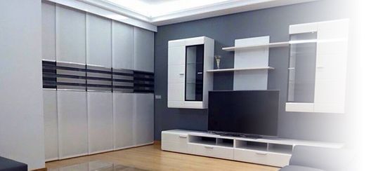 Sala de estar moderna con paneles de pared grises, estanterías empotradas, mueble de TV blanco y televisor grande.