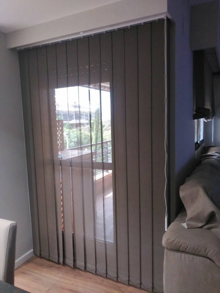 Puerta del salón con persianas verticales parcialmente abierta a un balcón con vistas