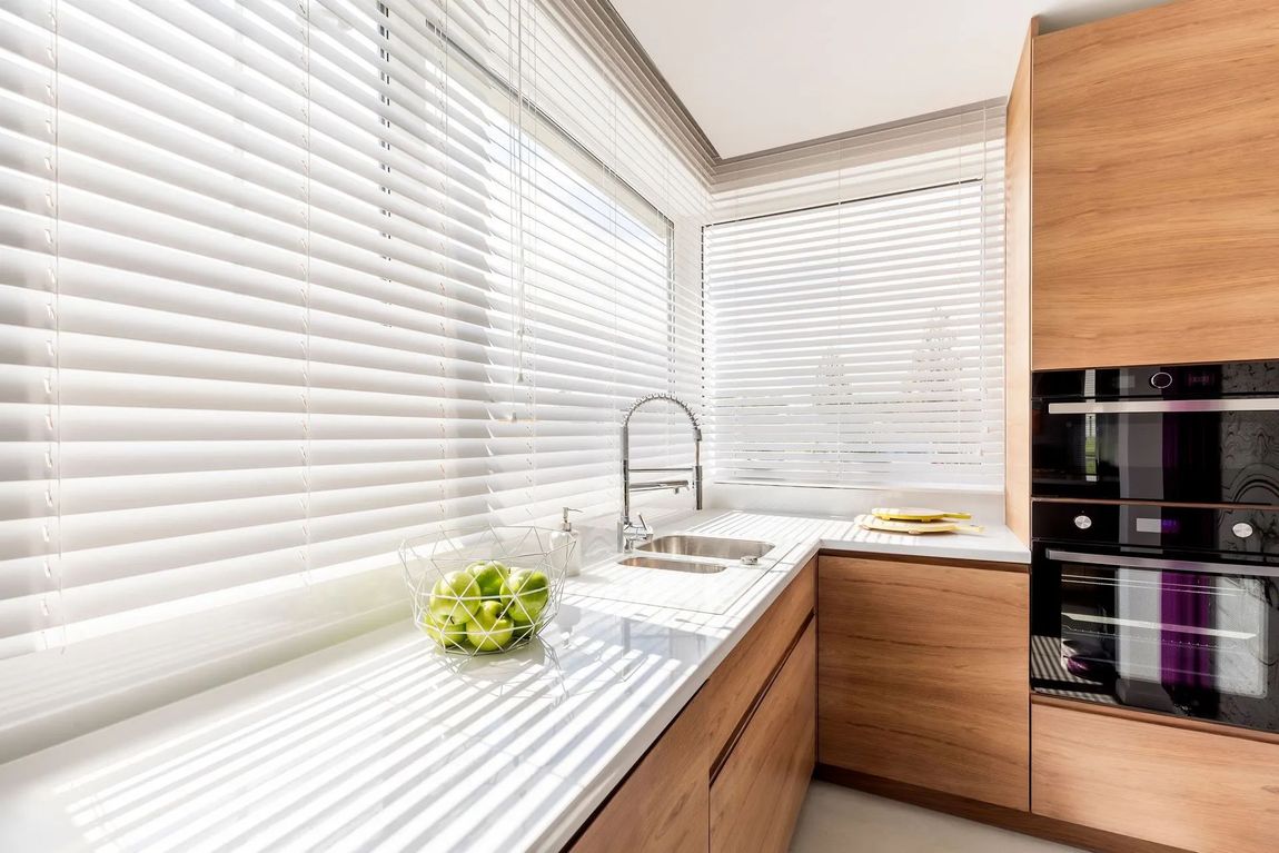 Cuisine moderne en bois avec plan de travail blanc et grandes fenêtres avec stores