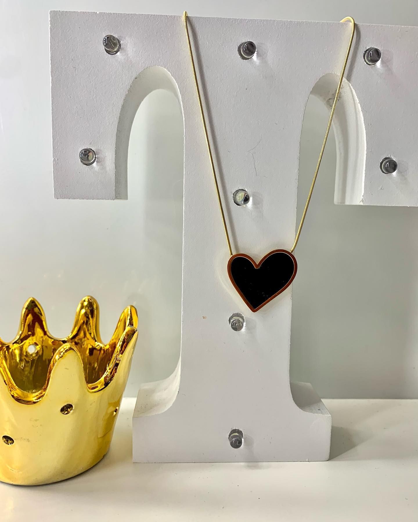 Una letra t blanca con un collar de corazón y una corona dorada.