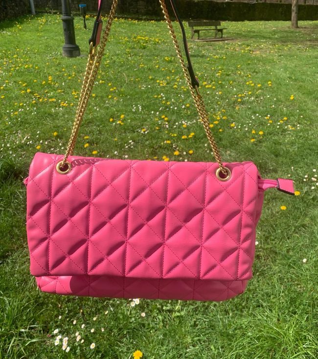Un bolso rosa con una cadena dorada se encuentra encima de un exuberante campo verde.