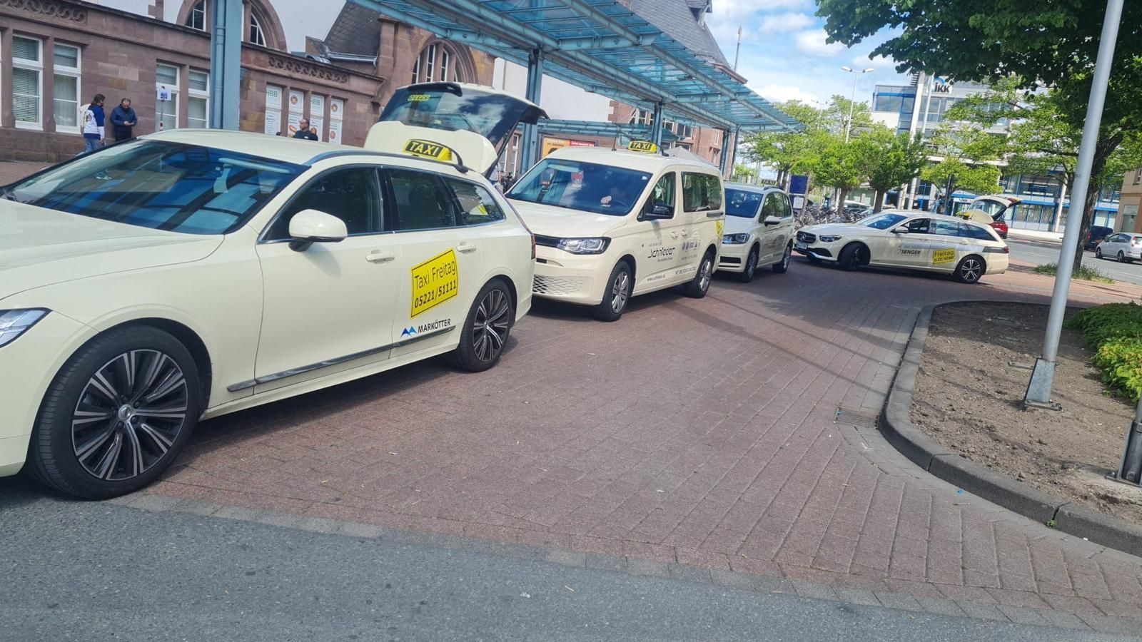 Eine Reihe weißer Taxis wartete auf einer Straße neben einem Backsteingebäude und einem überdachten Gehweg.