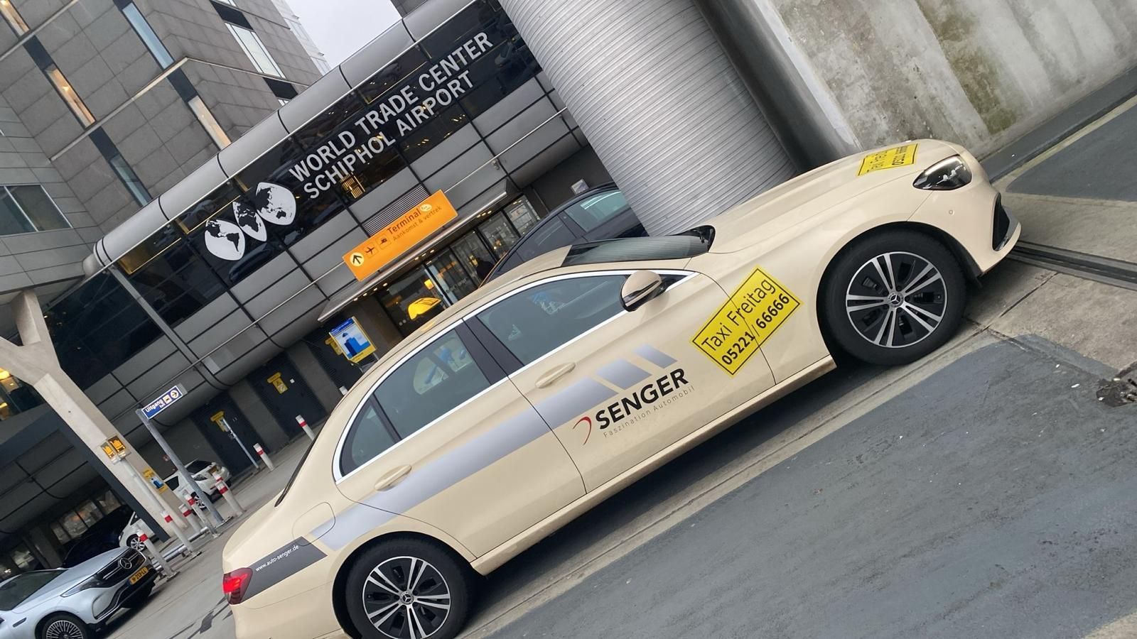 Ein beigefarbenes Limousinentaxi parkt vor dem Eingang eines Gebäudes mit schwarz-gelber Beschilderung.