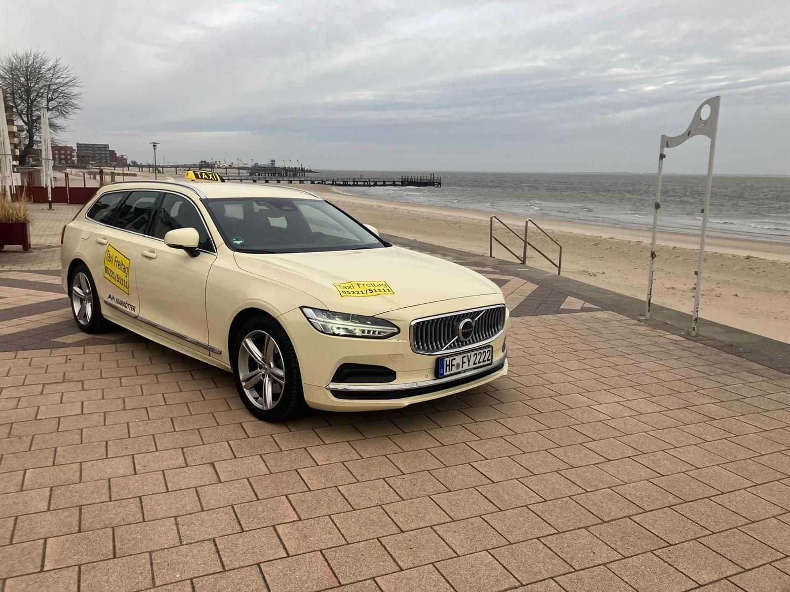 Beigefarbene BMW-Limousine parkt auf einer Strandpromenade unter bedecktem Himmel