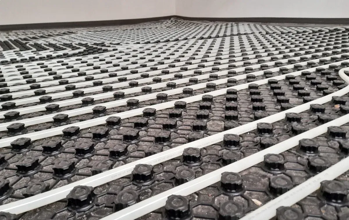 Tuberías de calefacción blancas instaladas en forma de cuadrícula sobre paneles aislantes de suelo moldeados de color negro