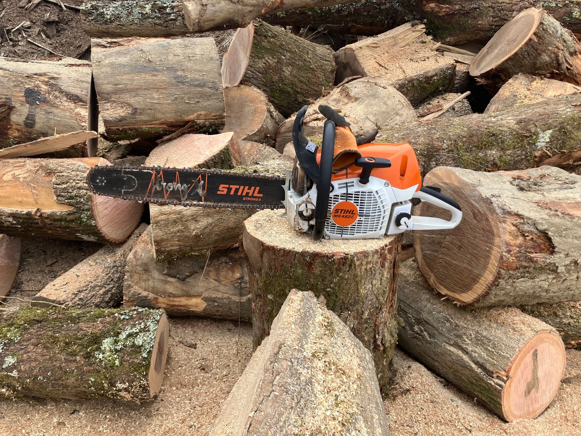 Tronçonneuse STIHL orange posée sur des bûches coupées empilées à l'extérieur.