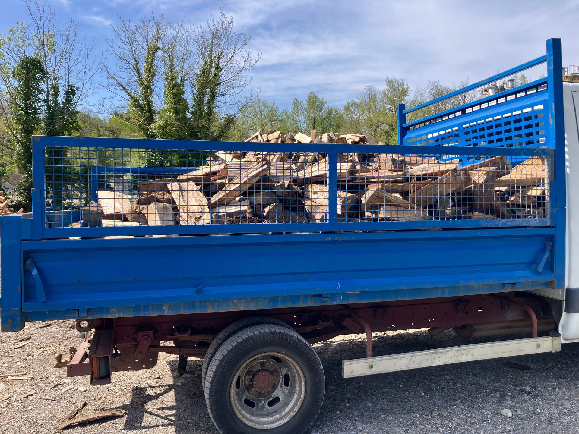 Une remorque bleue à plateau chargée de bois de rebut, garée à l'extérieur sous un ciel dégagé.