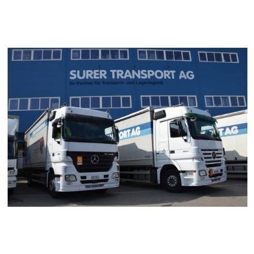 Zwei weisse Lkw der Surer Transport AG parkten vor einem blauen Firmengebäude.