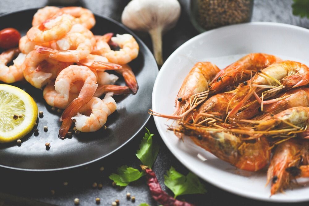 Un plato de camarones al lado de un plato de camarones cocidos.
