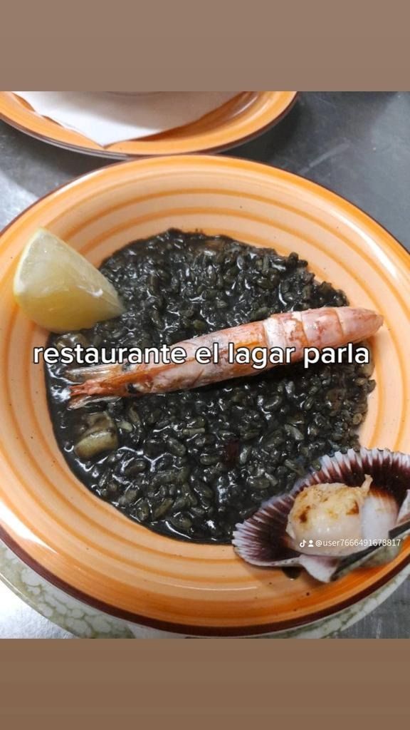 Un tazón de arroz negro con camarones y vieiras en una mesa.