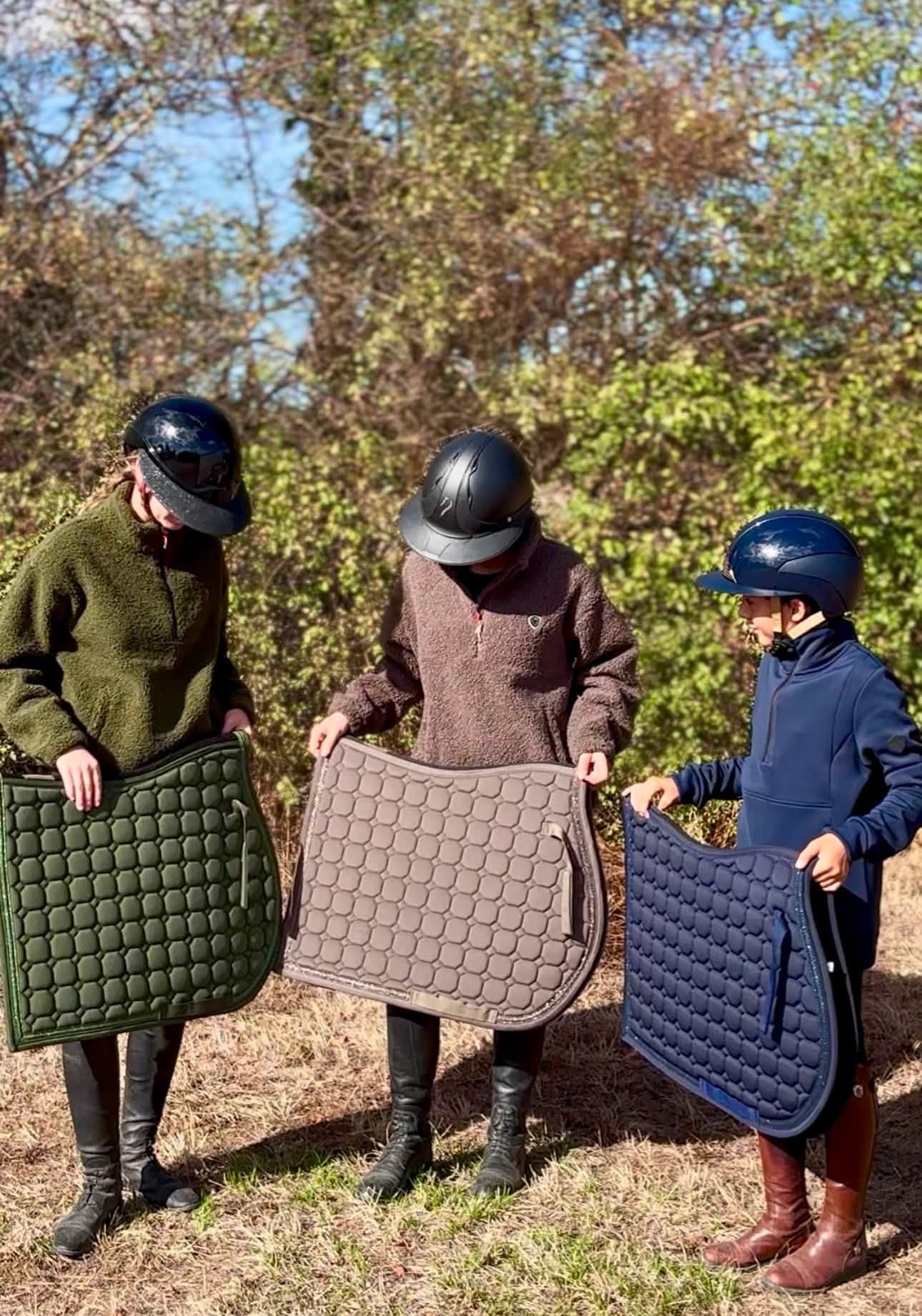 Trois personnes en extérieur tenant des tapis de selle matelassés pour chevaux, verts, beiges et bleu marine
