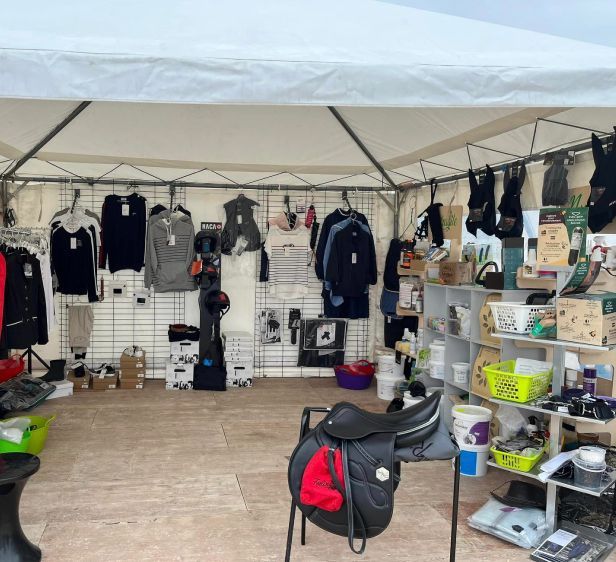 Stand de marché en plein air présentant des vêtements, des sacs et des accessoires noirs sous une tente blanche