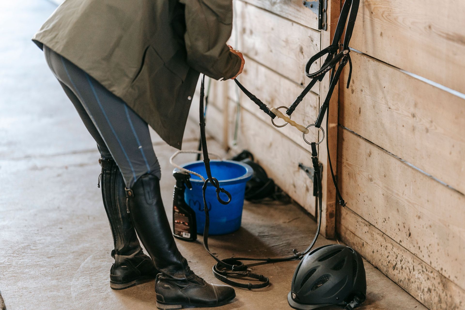 Une personne nettoie le matériel d’équitation d’un cheval contre le mur d’une écurie.
