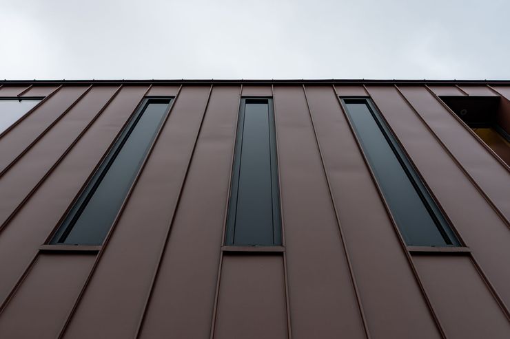 Façade d'un immeuble de grande hauteur avec des panneaux bruns et d'étroites fenêtres verticales, vue d'en bas