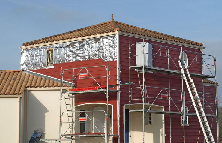 Maison en rénovation avec des échafaudages rouges et une échelle à l'extérieur