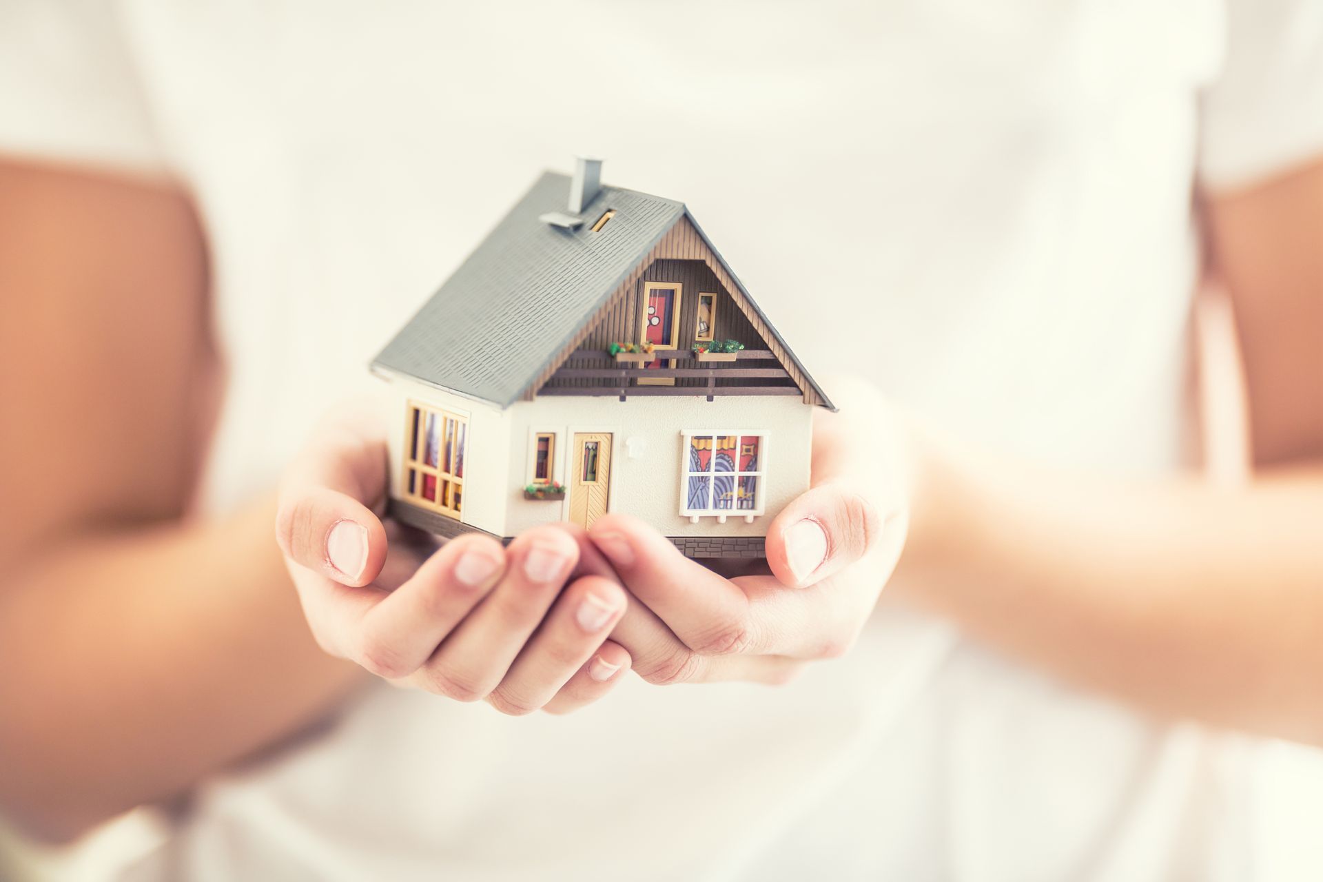 Des mains tenant une maquette de petite maison sur fond lumineux