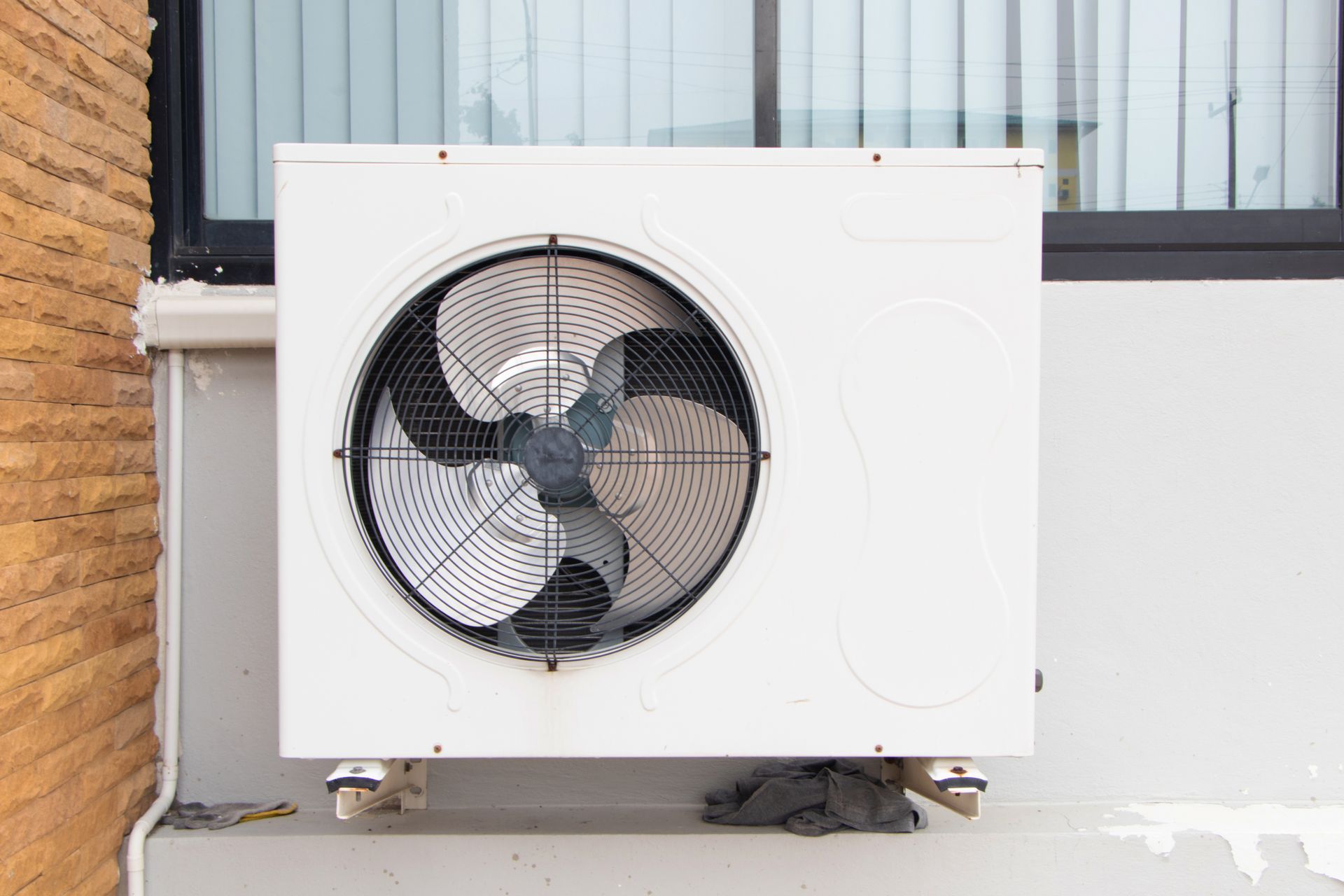 Unité de climatisation extérieure blanche avec ventilateur, fixée contre un mur de bâtiment