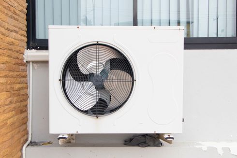 Unité de climatisation extérieure blanche avec ventilateur, fixée contre un mur de bâtiment