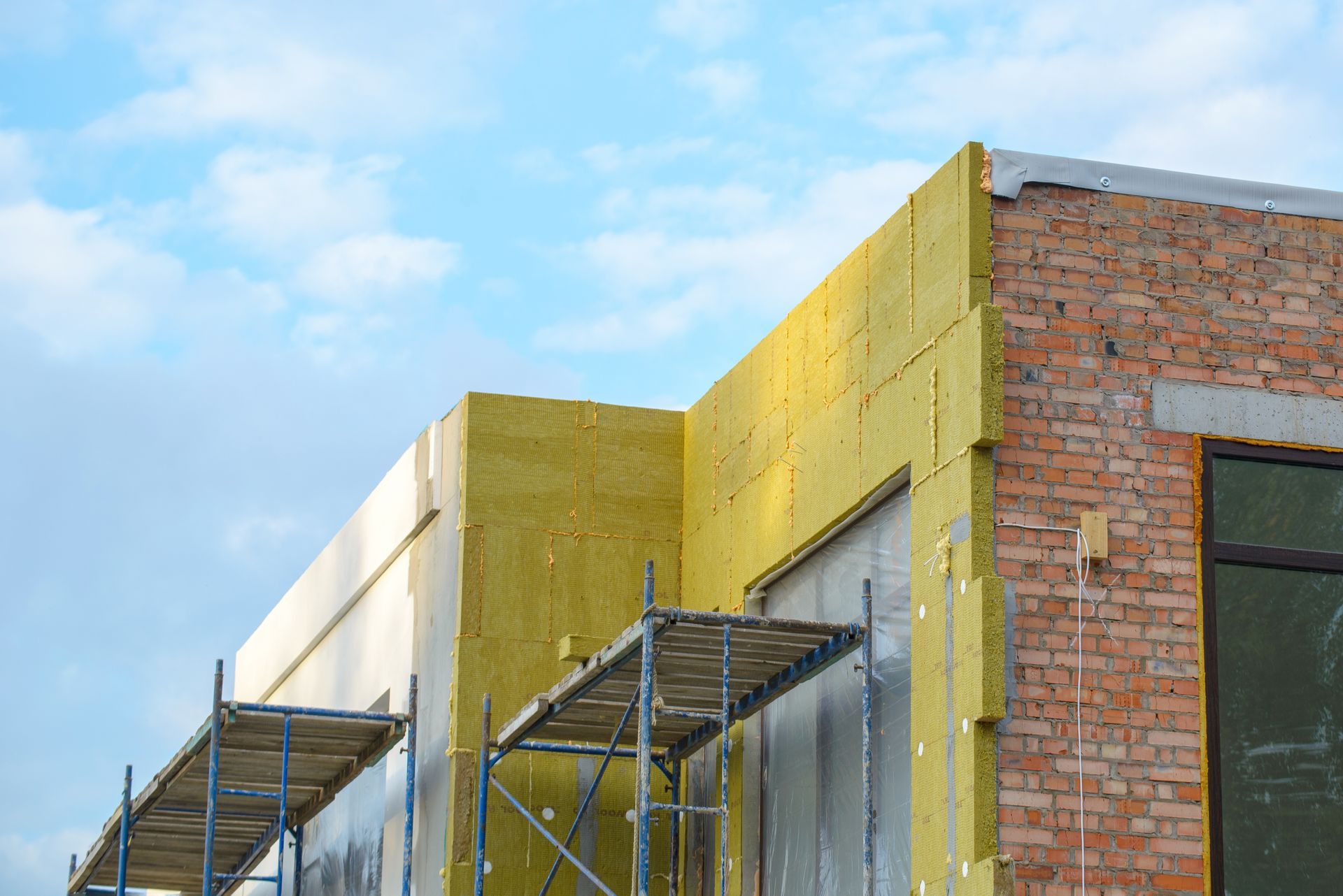 Chantier de construction avec échafaudages à côté de murs en briques et en plaques de plâtre jaune sous un ciel bleu