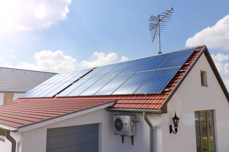 Toit de maison avec panneaux solaires bleus et antenne TV sous un ciel lumineux