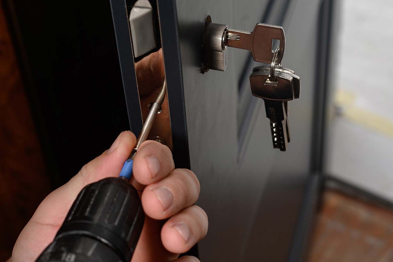 Una persona usa un taladro para instalar una cerradura con llaves en una puerta negra.