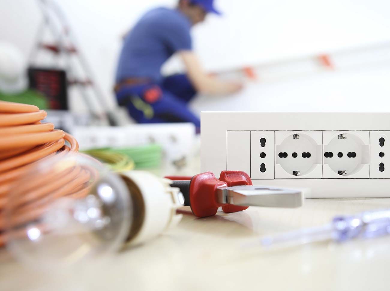Electricista instalando enchufes eléctricos; primer plano de herramientas y enchufes; fondo borroso del trabajador.