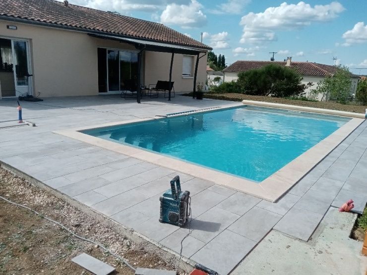 Espace piscine avec bassin turquoise, patio et maison beige sous un ciel bleu.