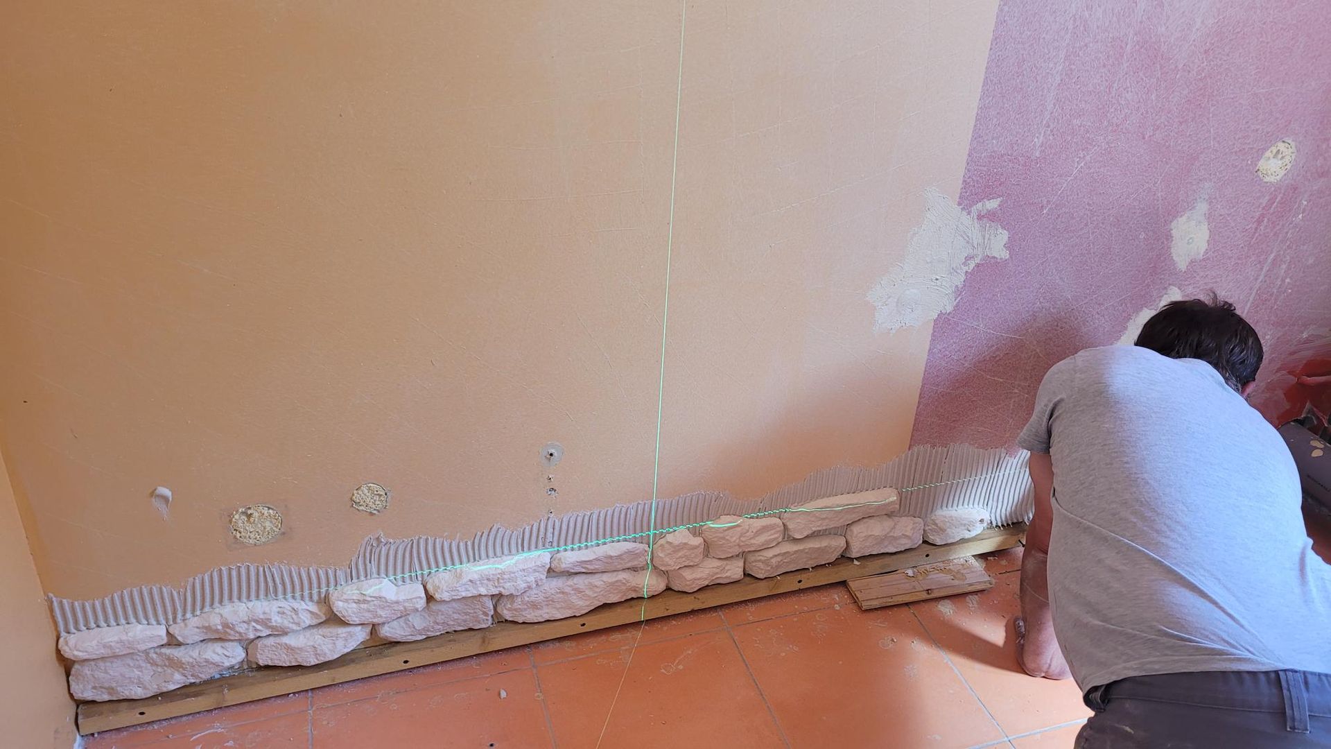 Personne installant un parement de briques sur un mur. Briques beiges, murs pêche et roses.