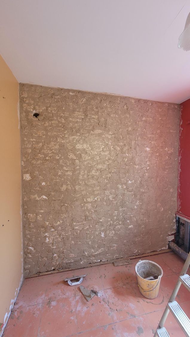 Pièce intérieure avec mur apparent en briques lors de la rénovation; des pots de peinture et une échelle sont présents.