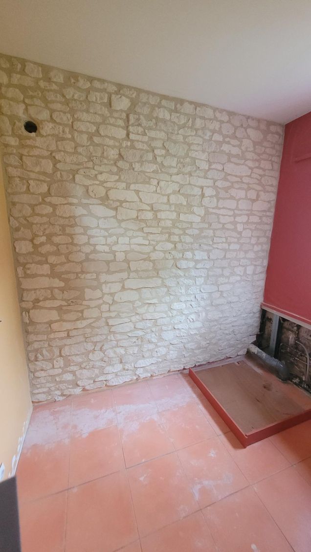 Mur en pierre, sol rouge orangé et mur rose. La pièce est inachevée.