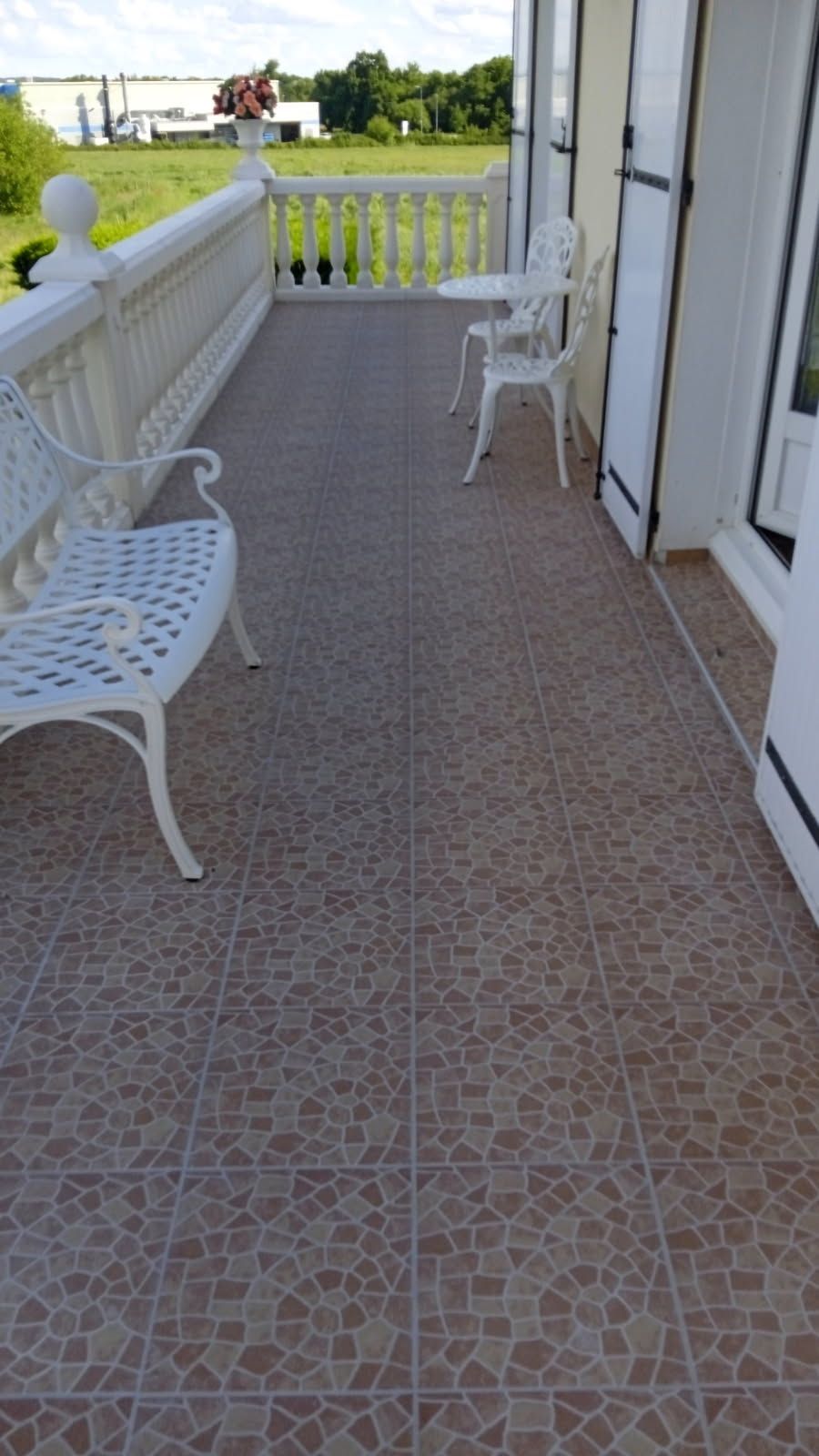Un balcon avec un banc blanc, des chaises et un sol carrelé donnant sur un champ.
