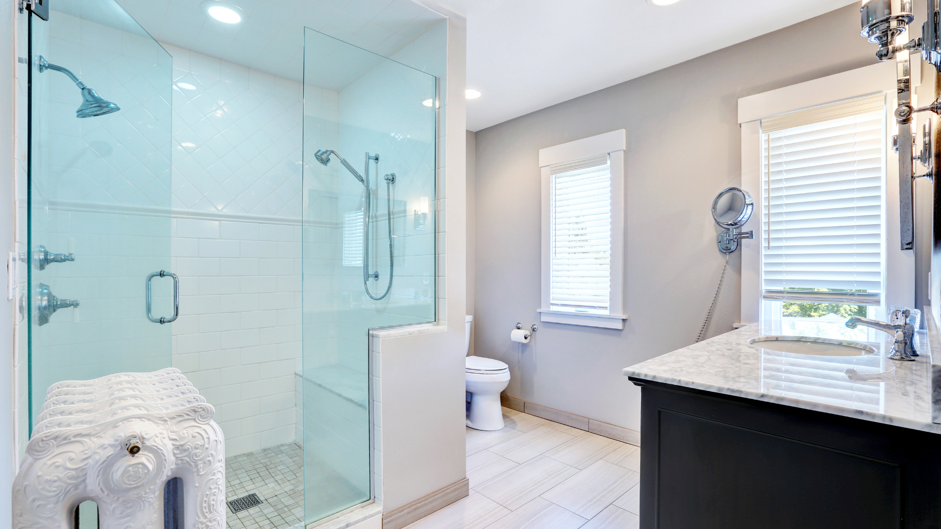 Salle de bain lumineuse avec douche en verre, toilettes, vanité et fenêtre avec stores.