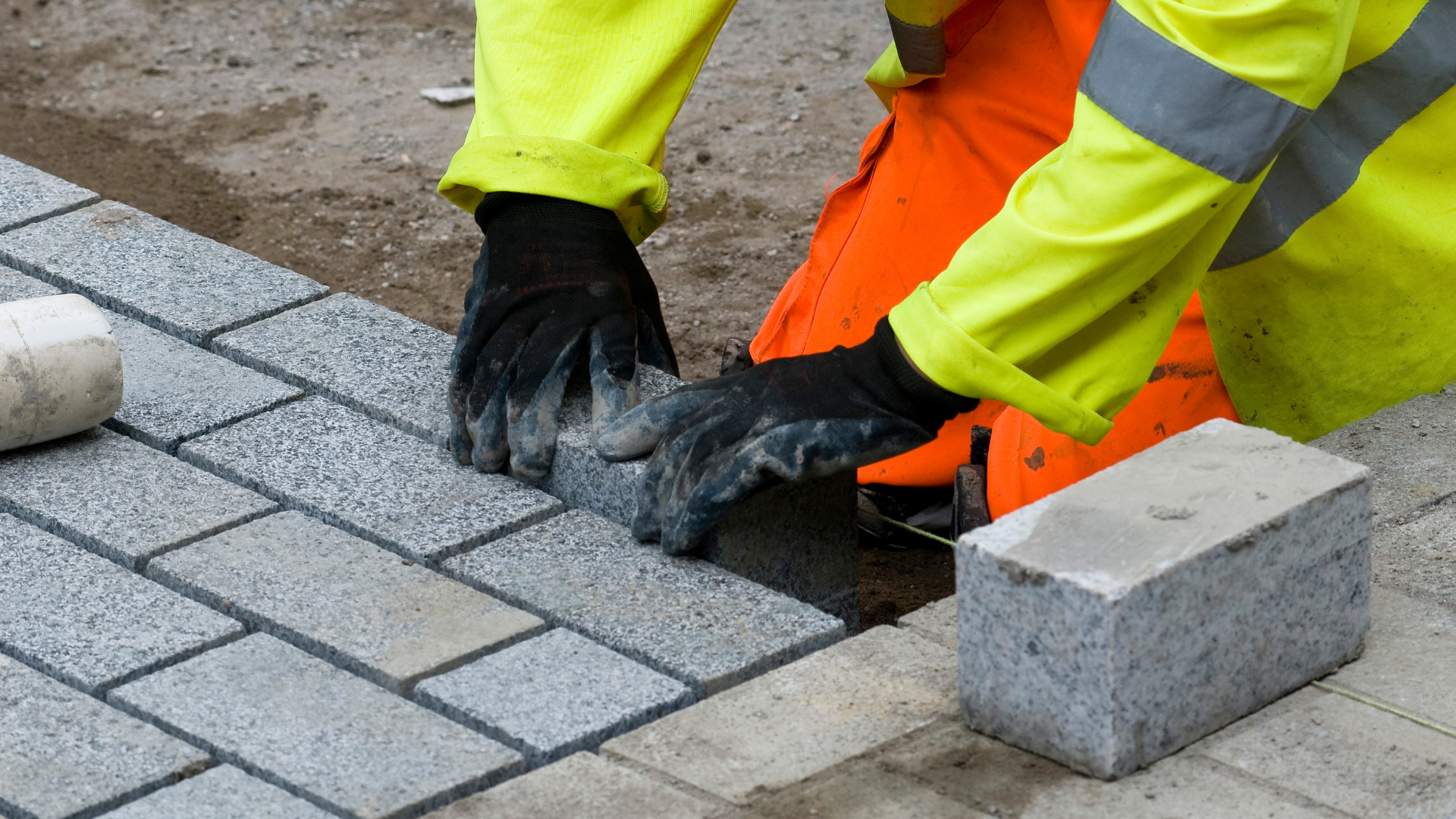 Une personne en vêtements de travail clairs pose des pavés gris.