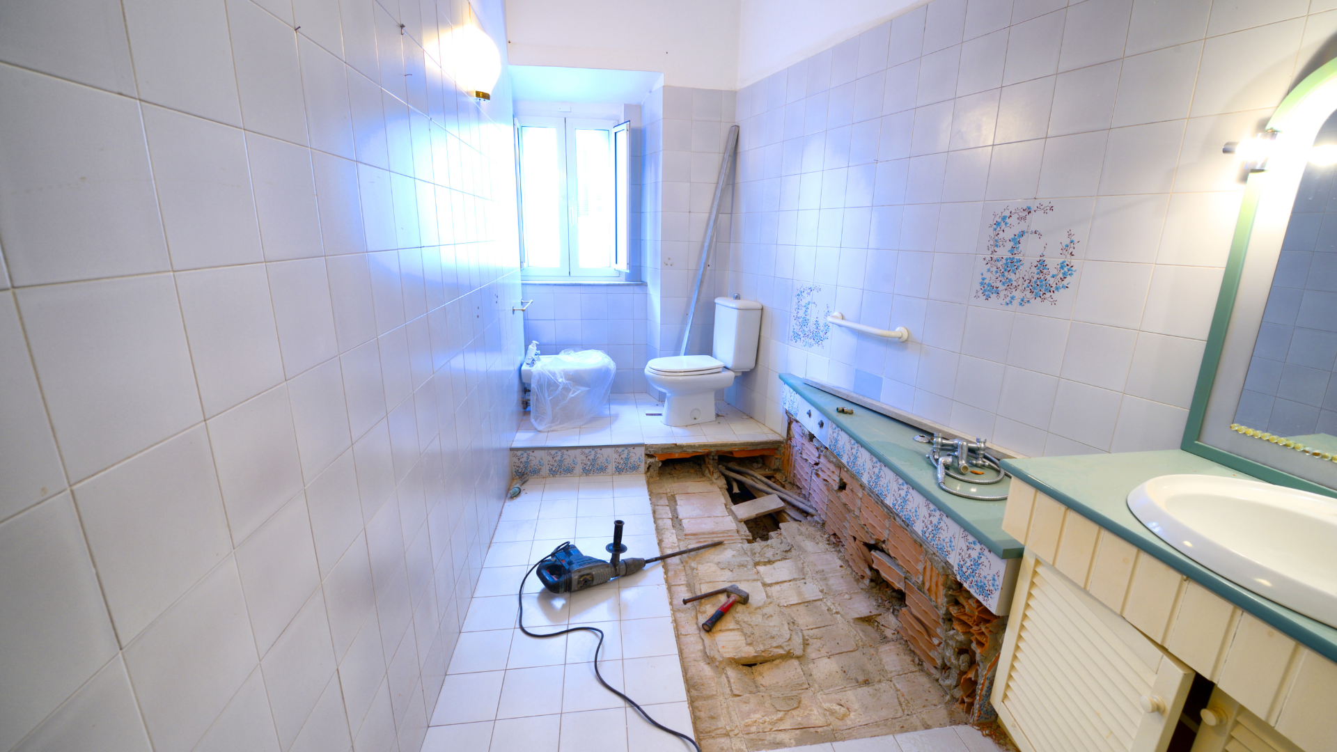 Salle de bain en cours de rénovation avec parquet apparent, carrelage blanc, toilettes et outils.