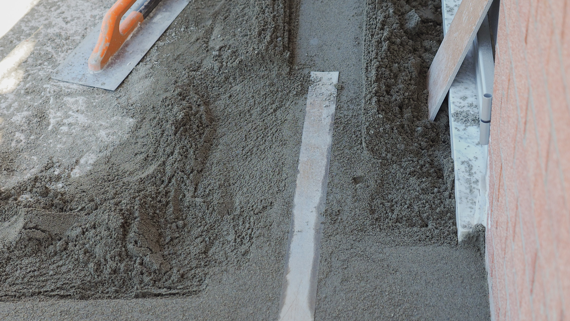Du ciment est étalé sur une surface à l'aide d'une truelle, une ligne blanche droite divisant la zone.