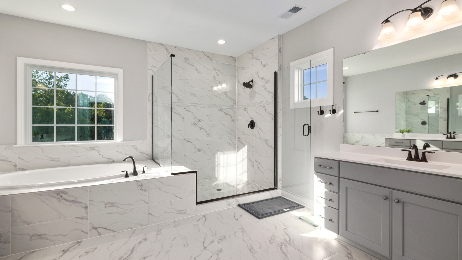 Salle de bain spacieuse et moderne avec carrelage en marbre, douche en verre, vanité grise et grande baignoire.