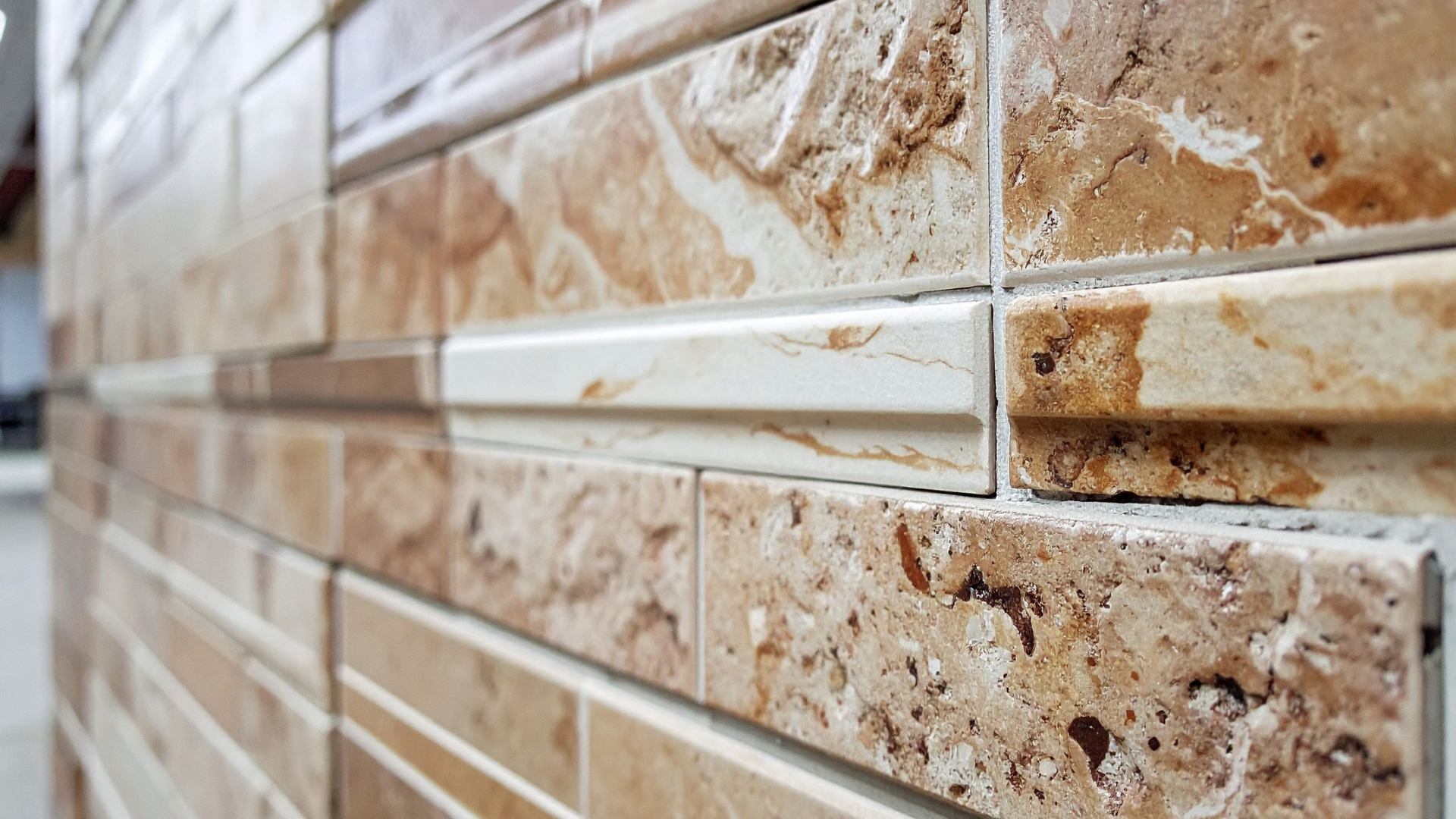 Gros plan d'un mur recouvert de carreaux de pierre beige et marron avec une bordure blanche contrastante.