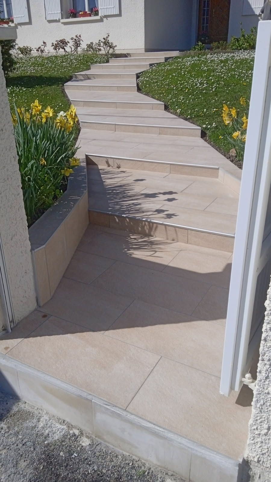 Marches en pierre menant à l'entrée d'un bâtiment avec de l'herbe verte et des fleurs jaunes à côté.